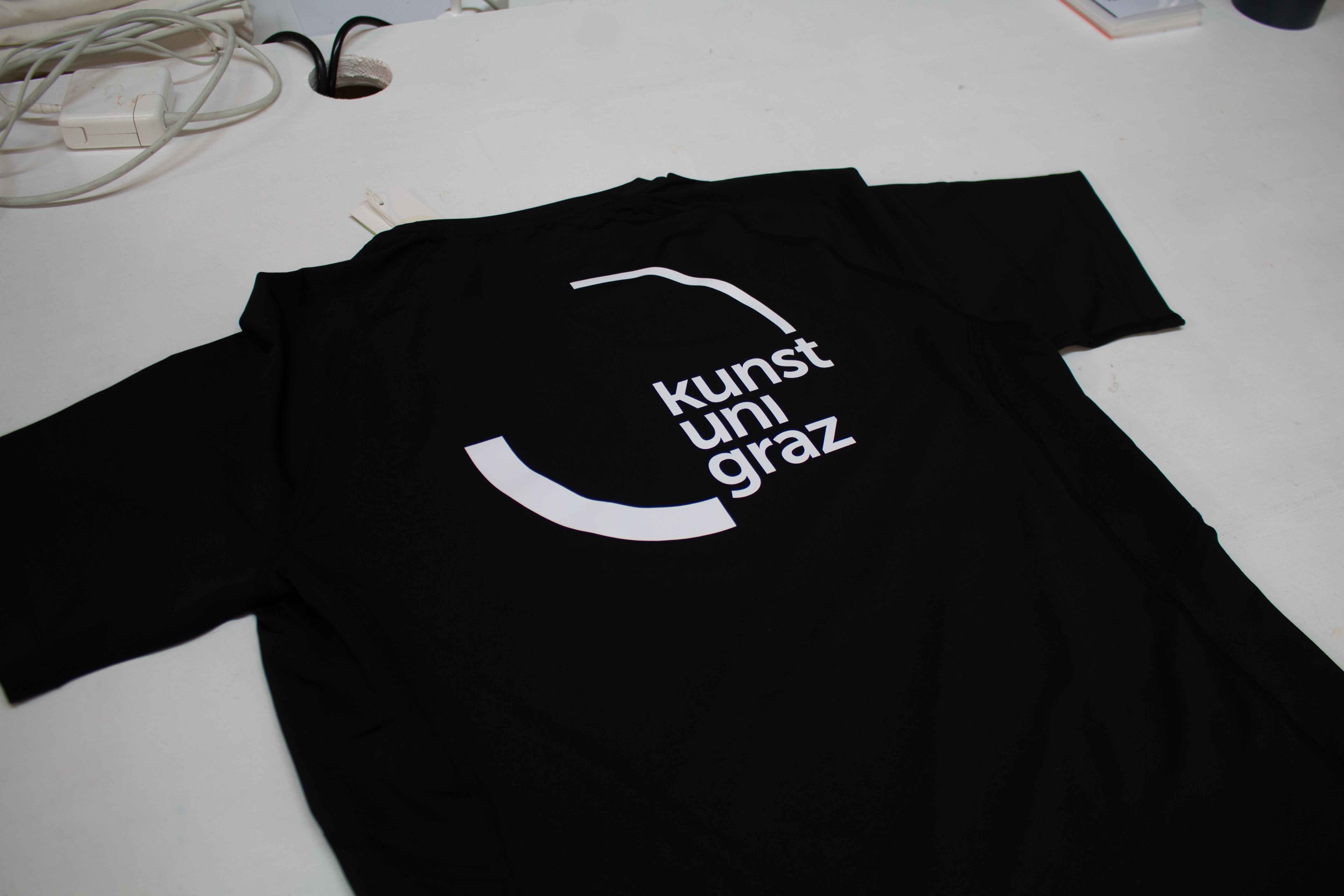 Siebdruck — schwarzes T-Shirt mit weißem Kunstuni-Graz-Logo, frisch gedruckt im Studio