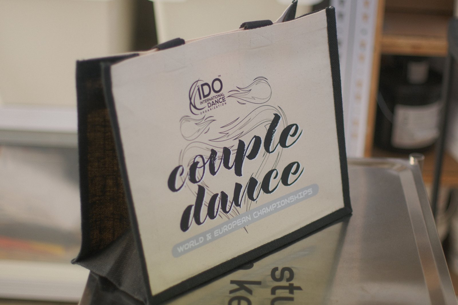 Westford Mill Jute-Shopper für die IDO Couple Dance World & European Championships — elegantes Schwung-Typografie-Motiv in Schwarz mit hellblauem Banner-Akzent im DTF-Druck