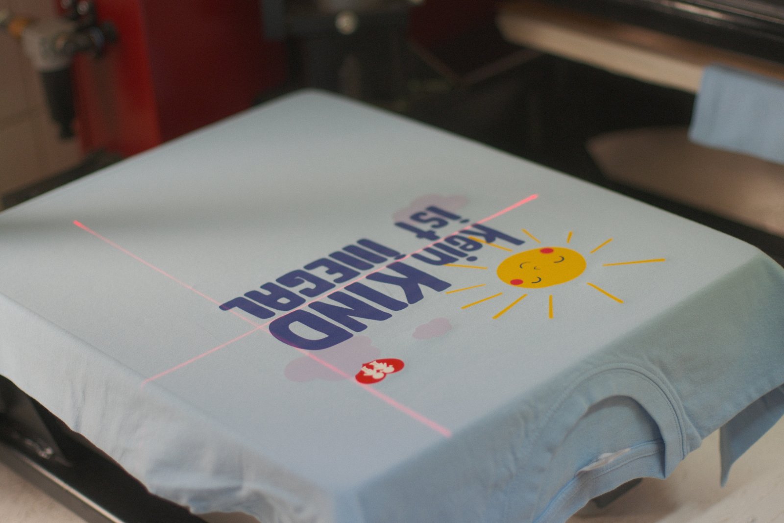 Hellblaues Kampagnen-Shirt im Siebdruck-Karussell mit Laser-Ausrichtung — Motiv 'Kein Kind ist illegal' wird in vier Farben gedruckt