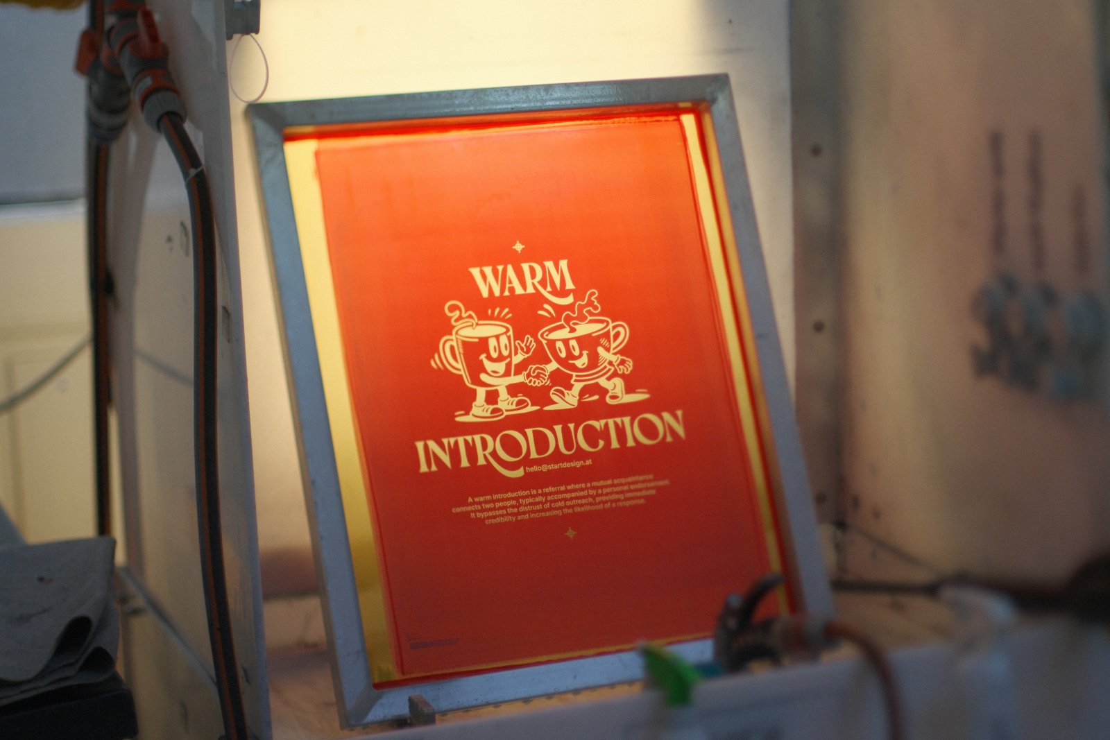 Belichtetes Siebdruck-Sieb mit Warm-Introduction-Motiv und zwei Tassen-Maskottchen für den Backprint der Start-Design-Auflage