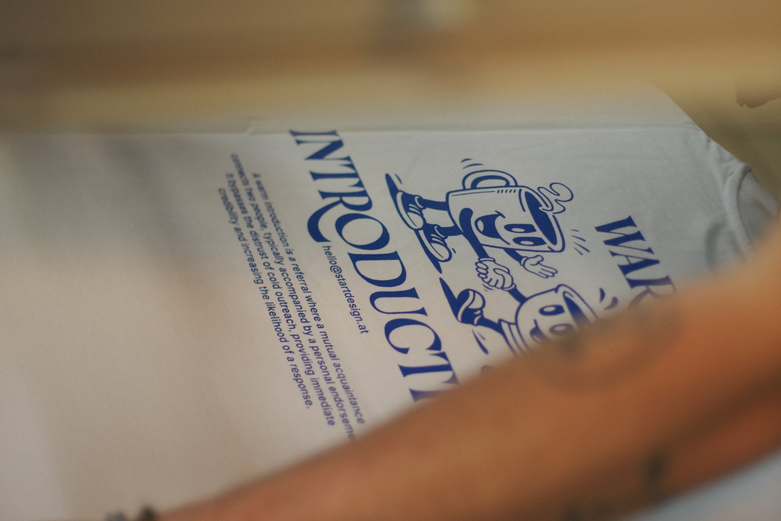 Detailaufnahme des Backprints — Typografie und Tassen-Illustration in Pantone 293 U auf naturweißem Oversized Boxy Tee
